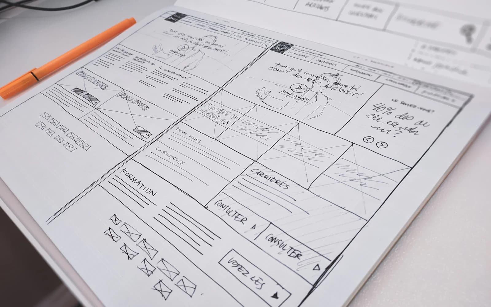 Website wireframe sketched on paper beside an orange pen.
